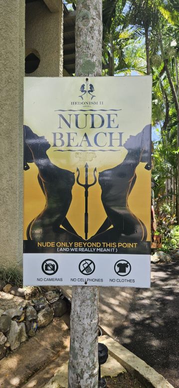 Nude beach sign with rules and sculpture imagery in background.