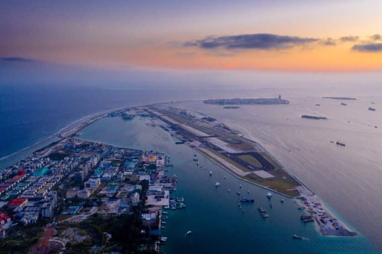 A stunning aerial view of a coastal city with sparkling blue waters, sandy beaches, and a bustling urban skyline at the horizon.