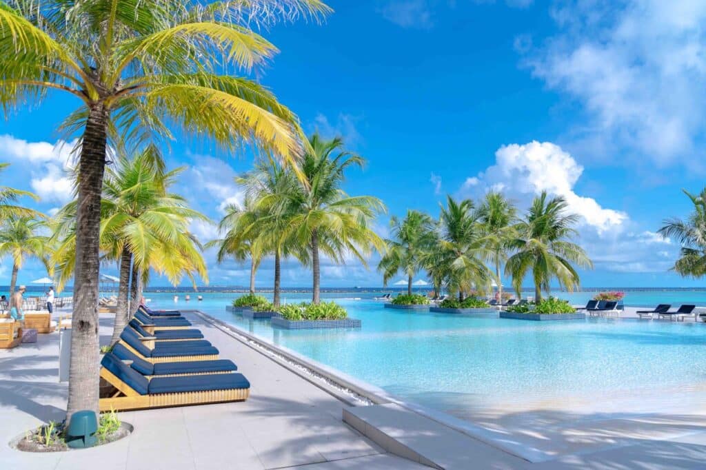 Luxurious poolside lounge with palm trees overlooking the crystal-clear ocean in the Maldives, perfect for a relaxing honeymoon retreat.